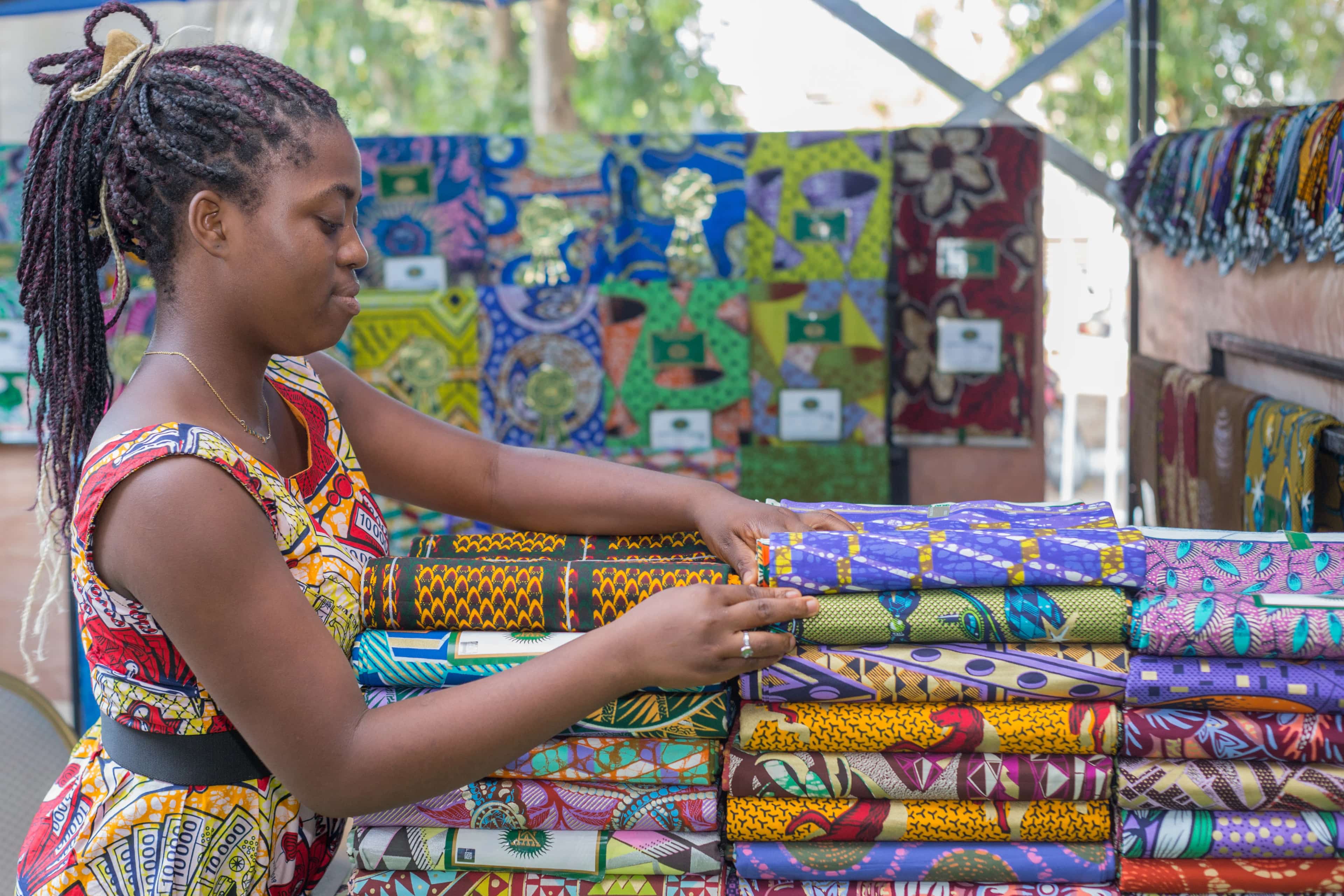 Une jeune femme range des pagnes colorés sur son étal
